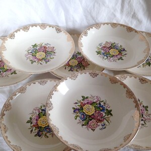 May include: Set of eight white ceramic soup bowls with a gold rim and floral design. Each bowl features a colorful bouquet of flowers in the center.