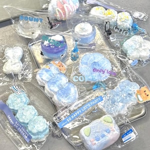 Puede incluir: Un surtido de objetos decorativos azules y blancos, incluyendo objetos con forma de nube y corazón, empaquetados en plástico transparente. Algunos artículos tienen texto como "COUNT" y "SO HAPPY LET'S PARTY".