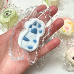 Chaveiro Taba Squishy: pingente artesanal em formato de pata de gato com carinha sorridente para aliviar o estresse.