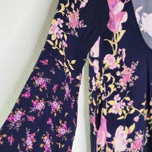 May include: Navy blue top with a floral pattern in pink, purple, and yellow. The top has long, bell sleeves and a scoop neckline. The floral print is scattered across the fabric.