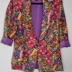 May include: A vintage blazer with a vibrant floral and paisley pattern in shades of pink, purple, yellow, and orange. The blazer has a purple lining and cuffs, and the label reads "Shane by Vistaloy".