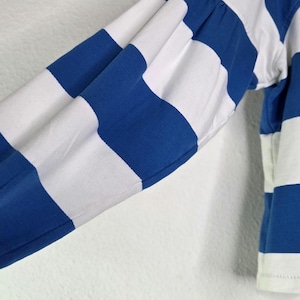 May include: Close-up of a long-sleeved shirt with blue and white horizontal stripes. The sleeve is gathered at the wrist with elastic. The shirt is made of a soft, comfortable material.