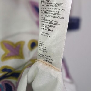 May include: A white fabric tag with text detailing the material composition of a garment. The tag lists percentages of cotton, linen, and polyester. The tag also includes the text "MADE IN INDIA".