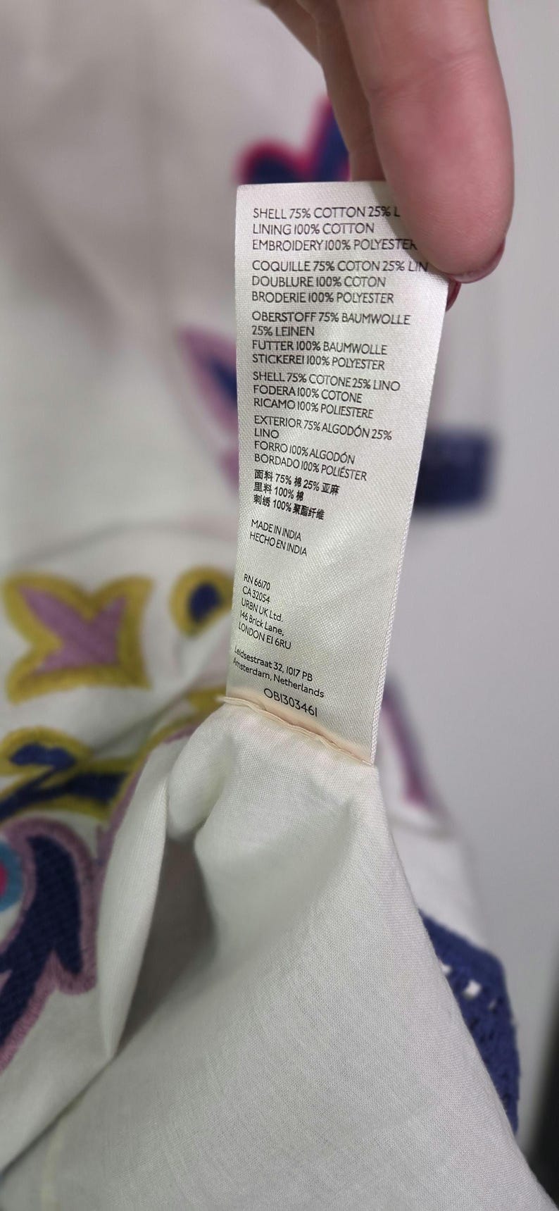 May include: A white fabric tag with text detailing the material composition of a garment. The tag lists percentages of cotton, linen, and polyester. The tag also includes the text "MADE IN INDIA".
