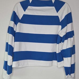 May include: A blue and white striped long-sleeve shirt. The shirt features horizontal stripes in alternating blue and white. The sleeves are long with a gathered cuff. The shirt is hanging on a white hanger.