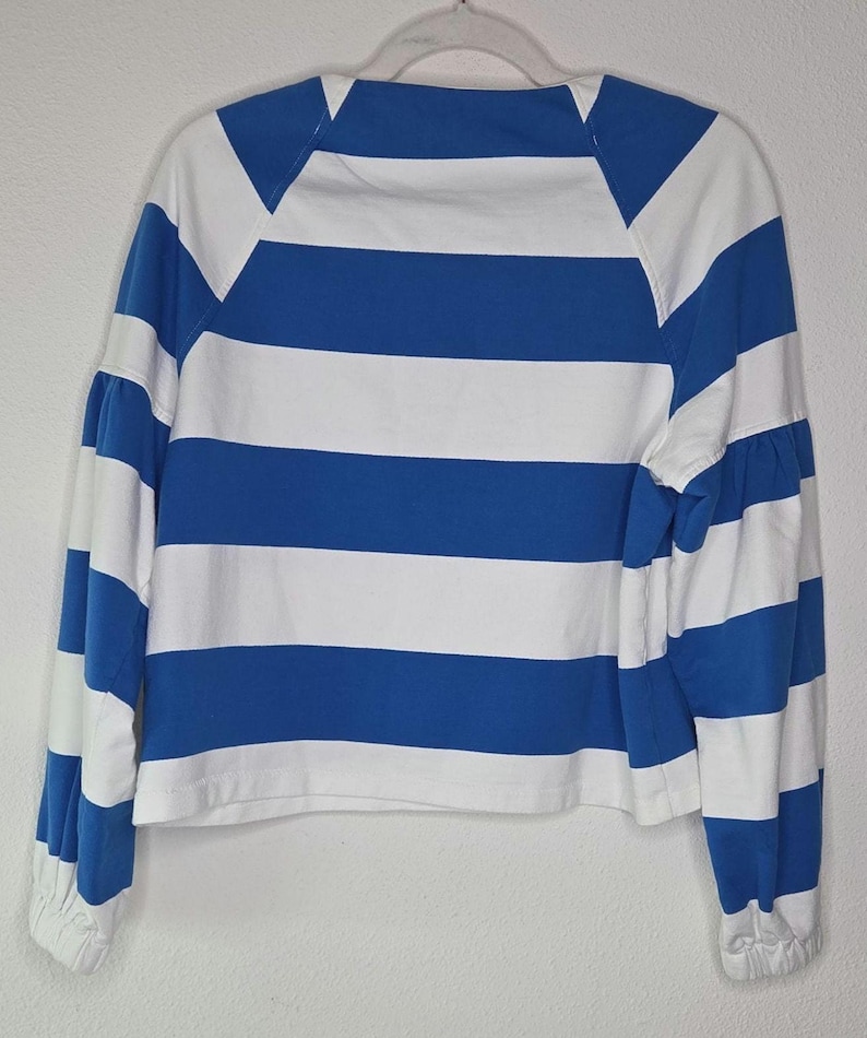 May include: A blue and white striped long-sleeve shirt. The shirt features horizontal stripes in alternating blue and white. The sleeves are long with a gathered cuff. The shirt is hanging on a white hanger.