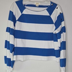 May include: A blue and white striped long-sleeve shirt. The shirt features wide horizontal stripes and a round neckline. The sleeves have a gathered, puffy design at the elbow and are cuffed at the wrist. The shoulder has three decorative buttons. The brand name "Maive" is visible.