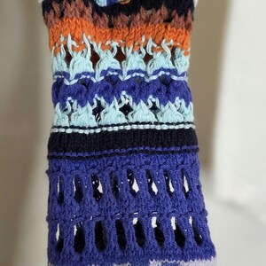 May include: Close-up of a colorful, patterned knitted sleeve. The design features a mix of white, orange, blue, and black sections. The lower portion has a blue and gray animal print.