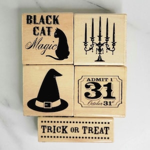 May include: A collection of wooden Halloween-themed stamps. Designs include a black cat with the words "Black Cat Magic", a candelabra, a witch's hat, the number 31 with "October 31st", and the phrase "Trick or Treat".