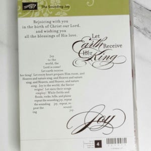 May include: A clear plastic case containing a stamp set. The cover features text that reads "The Sounding Joy" and "Let Earth Receive Her King." The design includes decorative flourishes and the word "Joy."