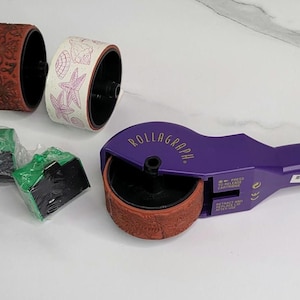May include: A purple Rollagraph tool with a brown roller is displayed alongside two patterned rollers and three green and black ink pads. One roller has a floral design, and the other has a seashell pattern.