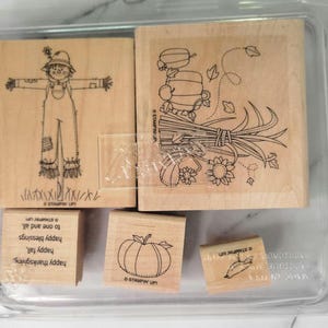 May include: A set of wooden stamps featuring fall-themed designs. The stamps include a scarecrow, a bundle of wheat, a pumpkin, and text that reads "Happy Thanksgiving, Happy Fall, Happy Blessings to one and all."
