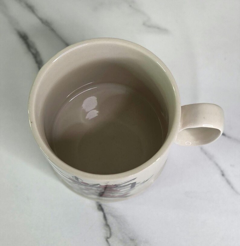 Puede incluir: Taza de cer&aacute;mica color crema con asa redondeada. El interior es de color beige claro y el exterior presenta un dise&ntilde;o sutil cerca de la base. La taza est&aacute; vac&iacute;a y se encuentra sobre una superficie de m&aacute;rmol blanco.