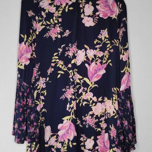 May include: A navy blue dress with a floral pattern in pink and purple, and yellow accents. The dress has long sleeves with a flared design and a high neckline. It is hanging on a hanger.