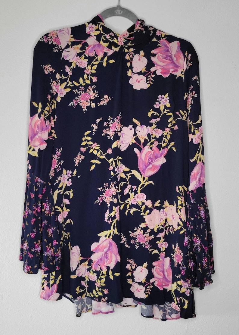 May include: A navy blue dress with a floral pattern in pink and purple, and yellow accents. The dress has long sleeves with a flared design and a high neckline. It is hanging on a hanger.