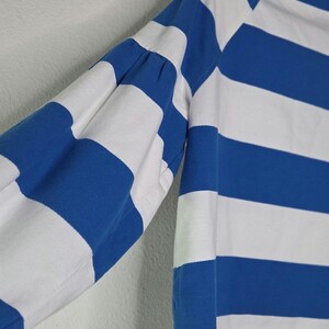 May include: A long-sleeved shirt with alternating horizontal stripes of white and blue. The sleeve is visible, showing the blue and white stripes. The shirt has a classic design, with a white collar and cuffs. The fabric appears to be a soft, breathable material.