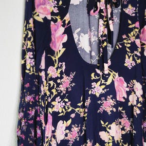 May include: A navy blue long-sleeved top with a floral pattern in pink and yellow. The top features a keyhole back and a tie at the neck. The floral print is spread across the entire top.