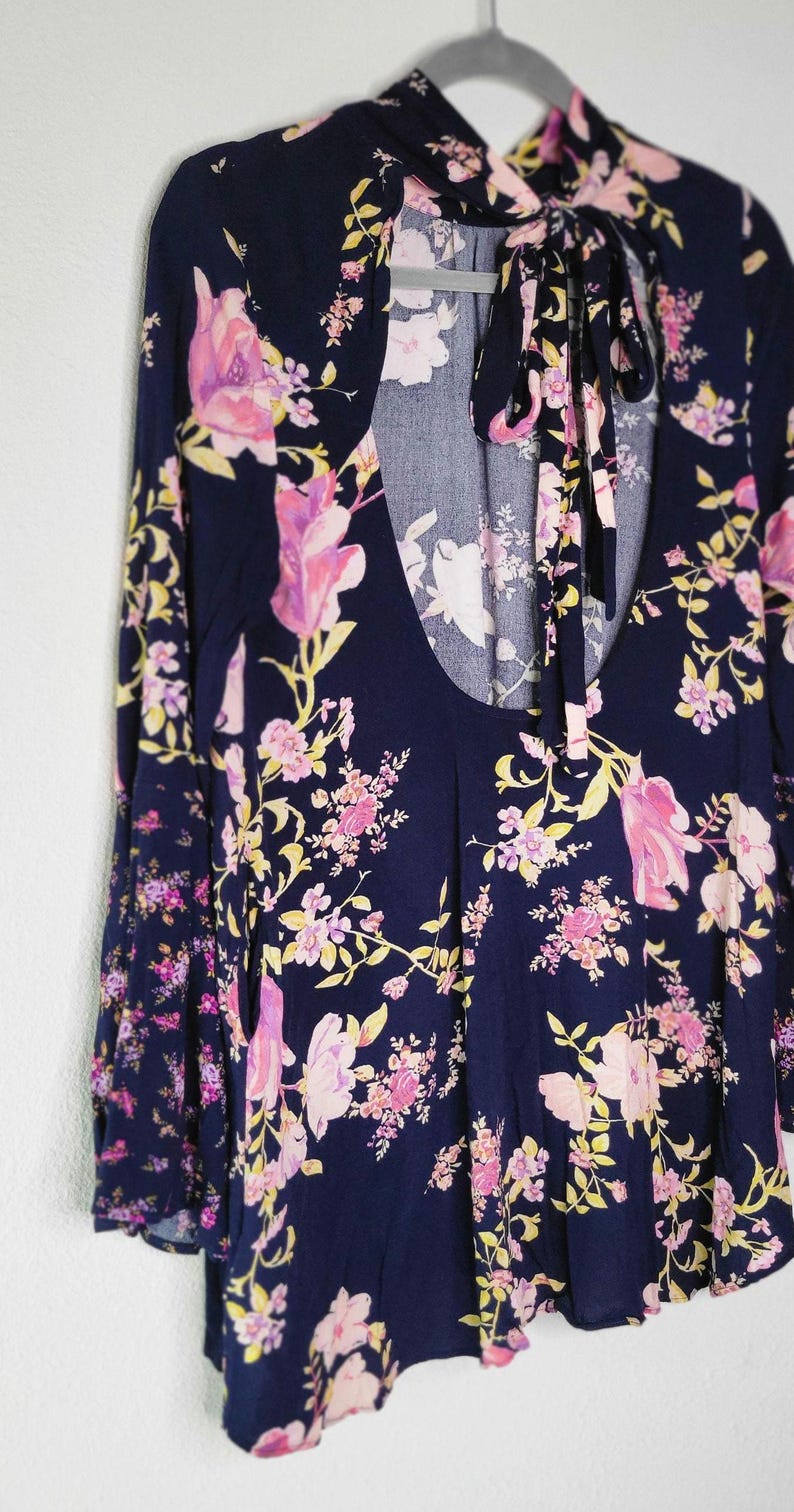 May include: A navy blue long-sleeved top with a floral pattern in pink and yellow. The top features a keyhole back and a tie at the neck. The floral print is spread across the entire top.