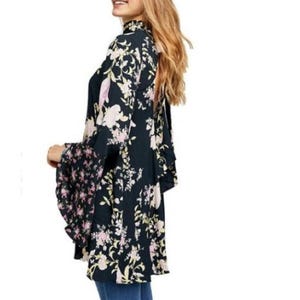 May include: A dark navy floral print kimono-style top with bell sleeves. The top features a high neckline and a mix of floral patterns in pink, cream, and green. The sleeves have a contrasting floral pattern.