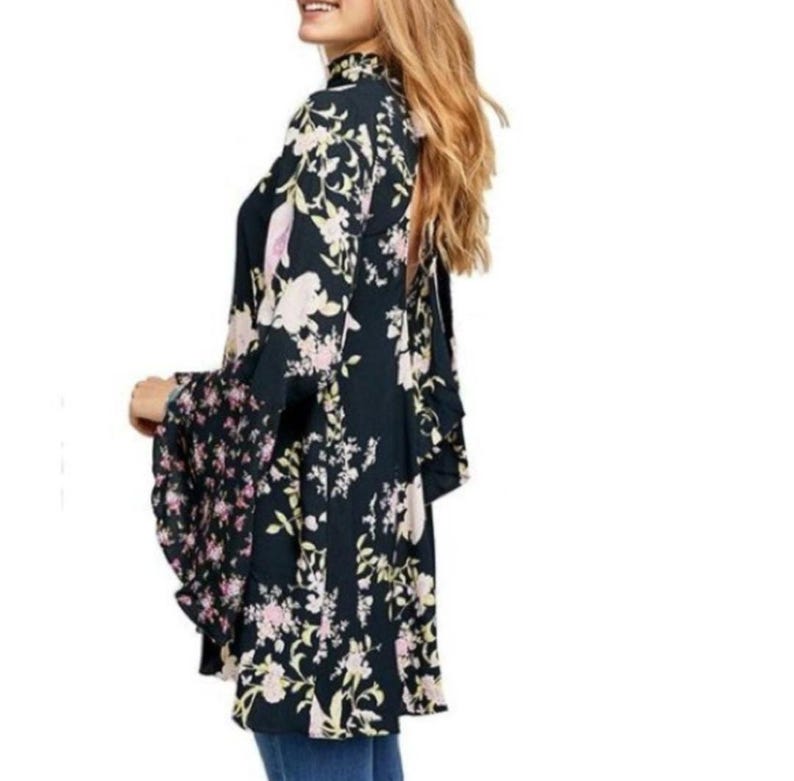 May include: A dark navy floral print kimono-style top with bell sleeves. The top features a high neckline and a mix of floral patterns in pink, cream, and green. The sleeves have a contrasting floral pattern.