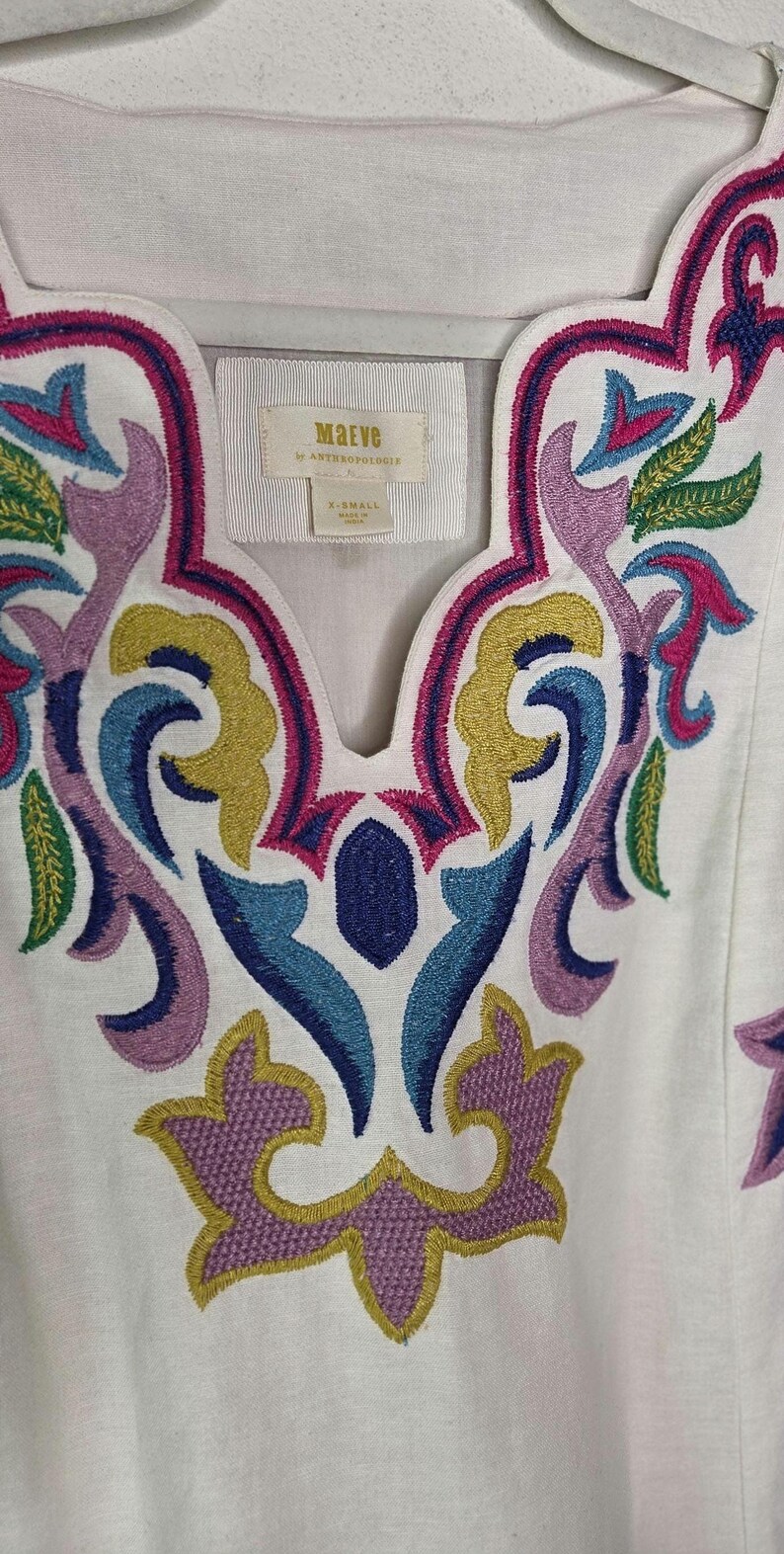 May include: White tunic top with colorful embroidered floral design. The embroidery features shades of pink, purple, blue, green, and yellow. The top has a scoop neckline and the brand name "Maeve" is visible on a tag.