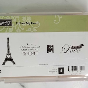 May include: Clear plastic case containing a stamp set. The set includes images of the Eiffel Tower, a key, and the words "Follow My Heart" and "True Love". The set is labeled "Stampin' Up!"