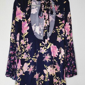 May include: A navy blue floral dress with long sleeves and a keyhole back. The dress features a pink and yellow floral pattern. The sleeves have a bell-shaped design. The dress is hanging on a grey hanger.