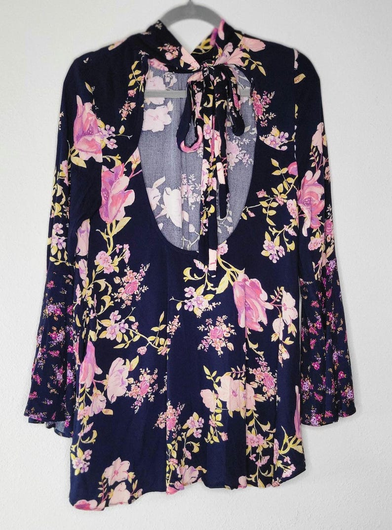 May include: A navy blue floral dress with long sleeves and a keyhole back. The dress features a pink and yellow floral pattern. The sleeves have a bell-shaped design. The dress is hanging on a grey hanger.