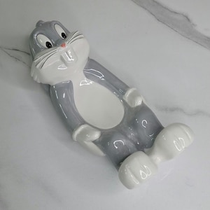 May include: A white ceramic mug with a black handle and the text "But First, Coffee" in a bold, black font. The mug is set against a neutral background, highlighting its simple design.