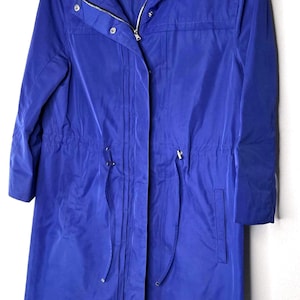 May include: A vibrant blue hooded coat with a zipper closure and drawstring waist. The coat has long sleeves and a tailored fit, hanging on a white hanger against a white background. The coat has a label that says "ELIE TAHARI."