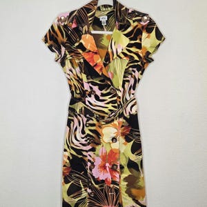 May include: A short-sleeved dress with a vibrant floral and animal print. The dress features a double-breasted design, a belted waist, and gold-toned buttons. The color palette includes black, yellow, orange, pink, and green.
