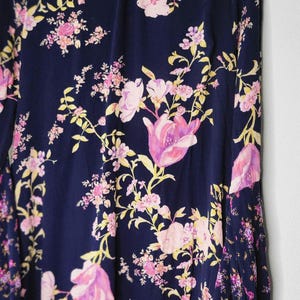 May include: A navy blue dress with a floral design. The dress has pink and yellow flowers and a high neckline. The long-sleeved dress is hanging on a grey hanger against a white background.
