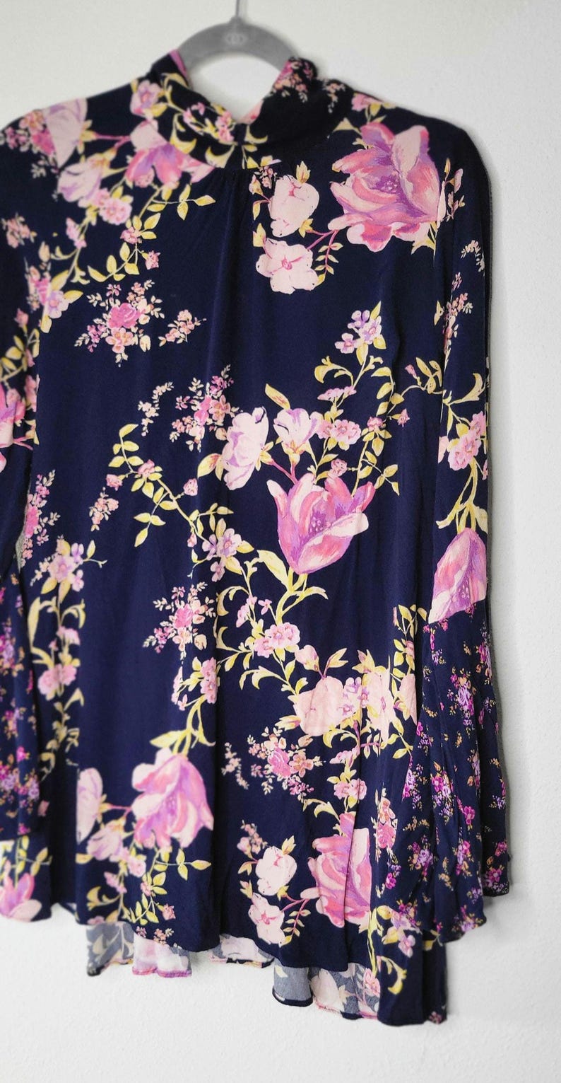 May include: A navy blue dress with a floral design. The dress has pink and yellow flowers and a high neckline. The long-sleeved dress is hanging on a grey hanger against a white background.
