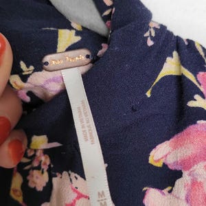 May include: Close-up of a navy blue floral top with pink and yellow flowers. The tag reads "Free People" and "Made in Vietnam". The top is size medium.