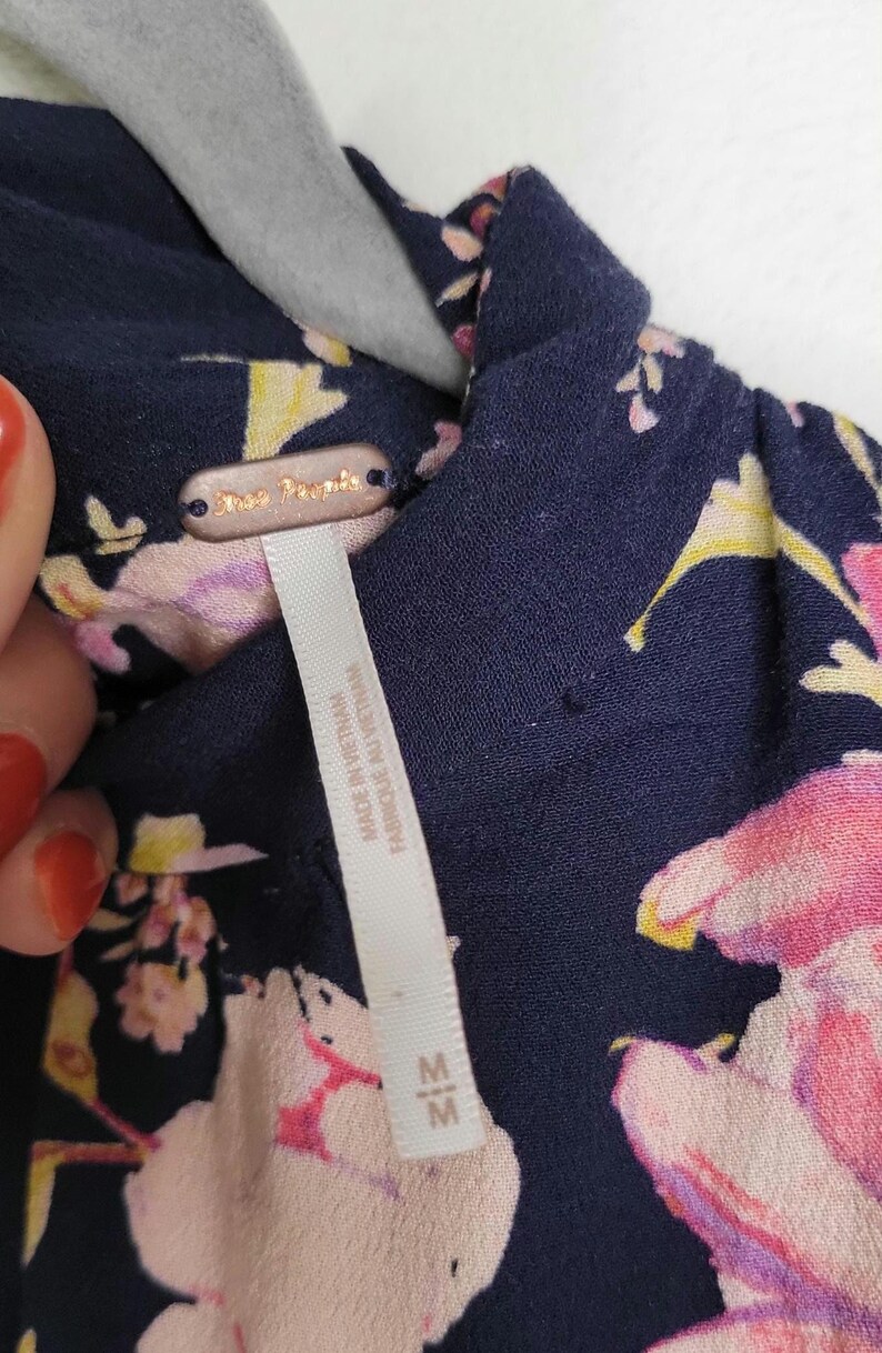 May include: Close-up of a navy blue floral top with pink and yellow flowers. The tag reads "Free People" and "Made in Vietnam". The top is size medium.