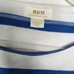 May include: Close-up of a blue and white striped top. The top features a label that reads "Maeve by Anthropologie" and indicates an X-Small size. The garment is made in India.