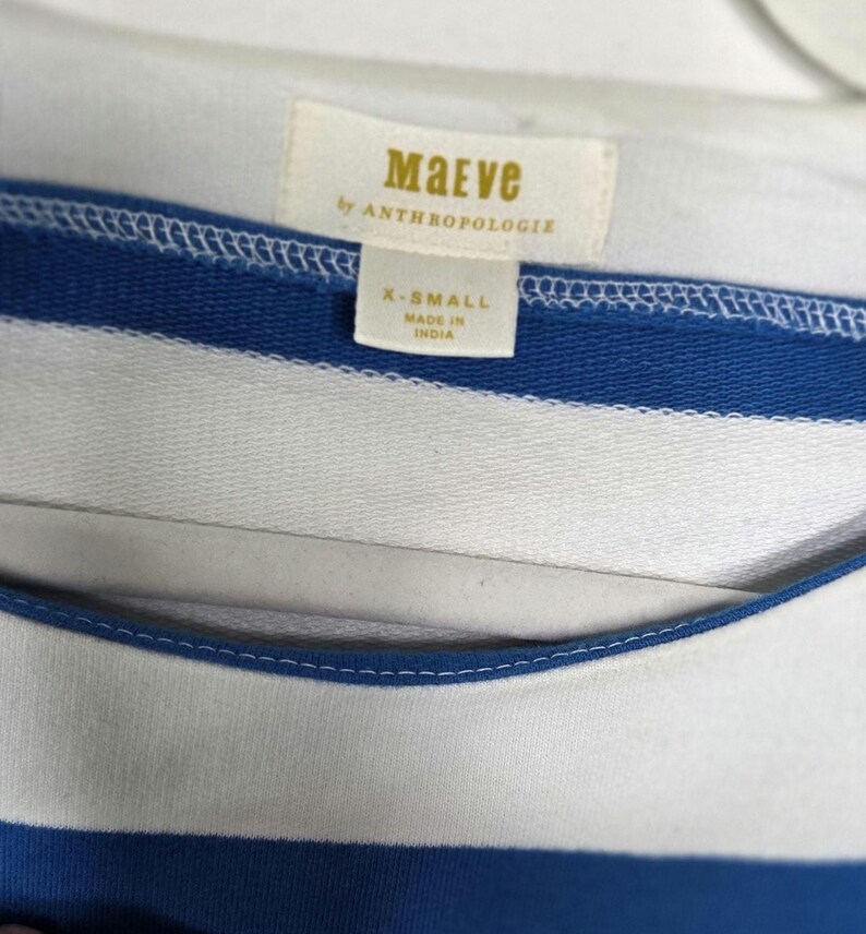 May include: Close-up of a blue and white striped top. The top features a label that reads "Maeve by Anthropologie" and indicates an X-Small size. The garment is made in India.