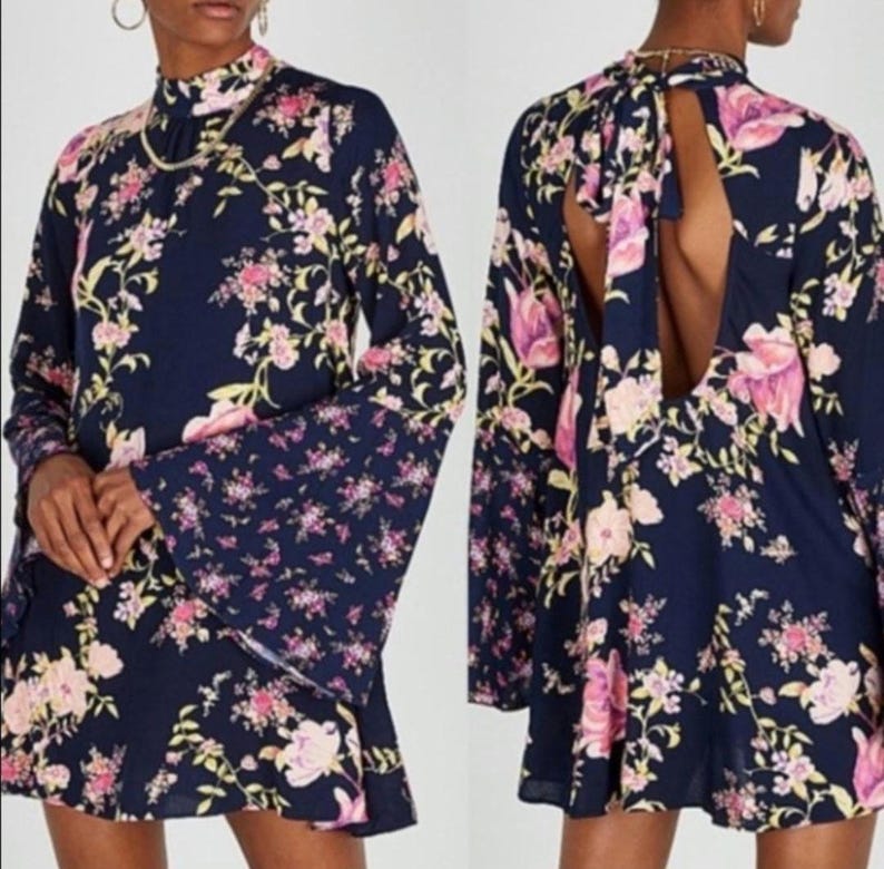 May include: A navy blue dress with a floral pattern in pink and yellow. The dress has long bell sleeves and a high neckline. The back of the dress has a keyhole opening. The dress is a mini length.