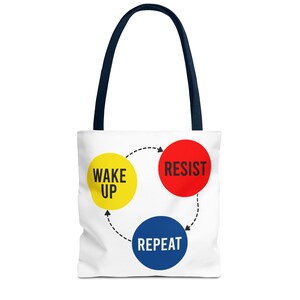 May include: White tote bag with navy blue handles. The bag features a circular graphic with the words "WAKE UP", "RESIST", and "REPEAT" in yellow, red, and blue, respectively, connected by a dotted line.