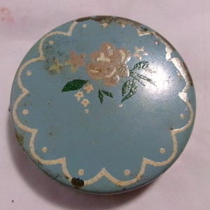 May include: A vintage blue and white compact with a floral design. The compact has a scalloped edge and a white trim.