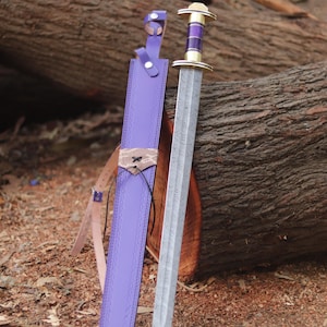 May include: A double-edged sword with a patterned steel blade and a purple and brass hilt, accompanied by a matching purple leather scabbard featuring a tan leather accent, black lacing, and adjustable straps with silver-toned metal buckles.