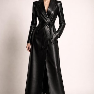 May include: A long, black leather trench coat with a belted waist and a notched collar. The coat has long sleeves and a front slit, and is worn with black boots. The coat is a classic, elegant style.