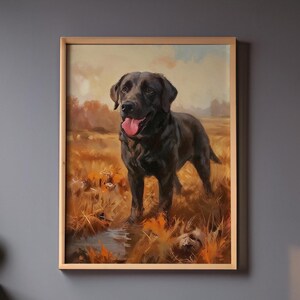 May include: A framed painting of a black Labrador Retriever standing in a field of tall, dry grass. The dog has its tongue out and is looking forward. The background features a stream and trees under a cloudy sky. The frame is made of light-colored wood.