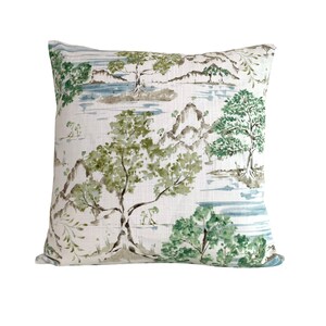 May include: A white cushion with a green and blue watercolour landscape design. The design features trees, mountains, and water.