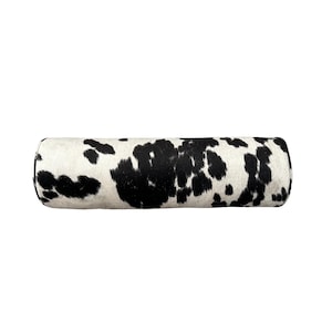 May include: A cylindrical decorative pillow with a cowhide pattern. The pillow features a white background with irregular black spots, creating a natural and rustic aesthetic. The pillow is designed for comfort and style.