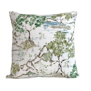 May include: A white cushion with a green and brown watercolour print of trees and a lake. The cushion has a subtle linen texture.