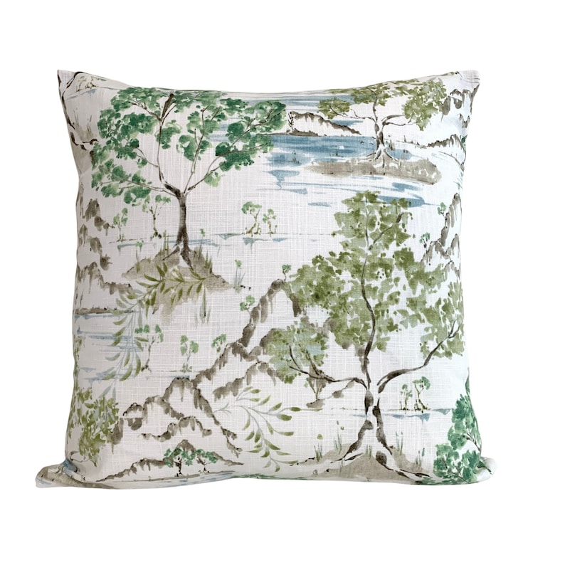 May include: A white cushion with a green and brown watercolour print of trees and a lake. The cushion has a subtle linen texture.