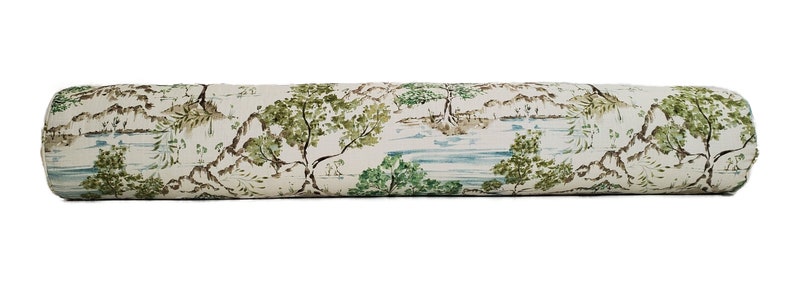 May include: A long, cylindrical cushion with a white background and a repeating pattern of green trees, brown mountains, and blue water. The cushion is ideal for adding a touch of nature to any room.