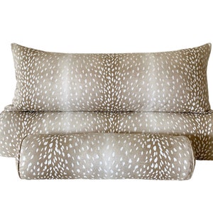May include: Three decorative pillows with a fawn print pattern. The pillows are in shades of brown and white. The largest pillow is a rectangular bolster pillow. The two smaller pillows are cylindrical bolster pillows.