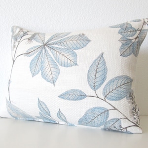 May include: A white throw pillow with a blue and gray leaf pattern. The pillow is made of a soft, textured fabric.